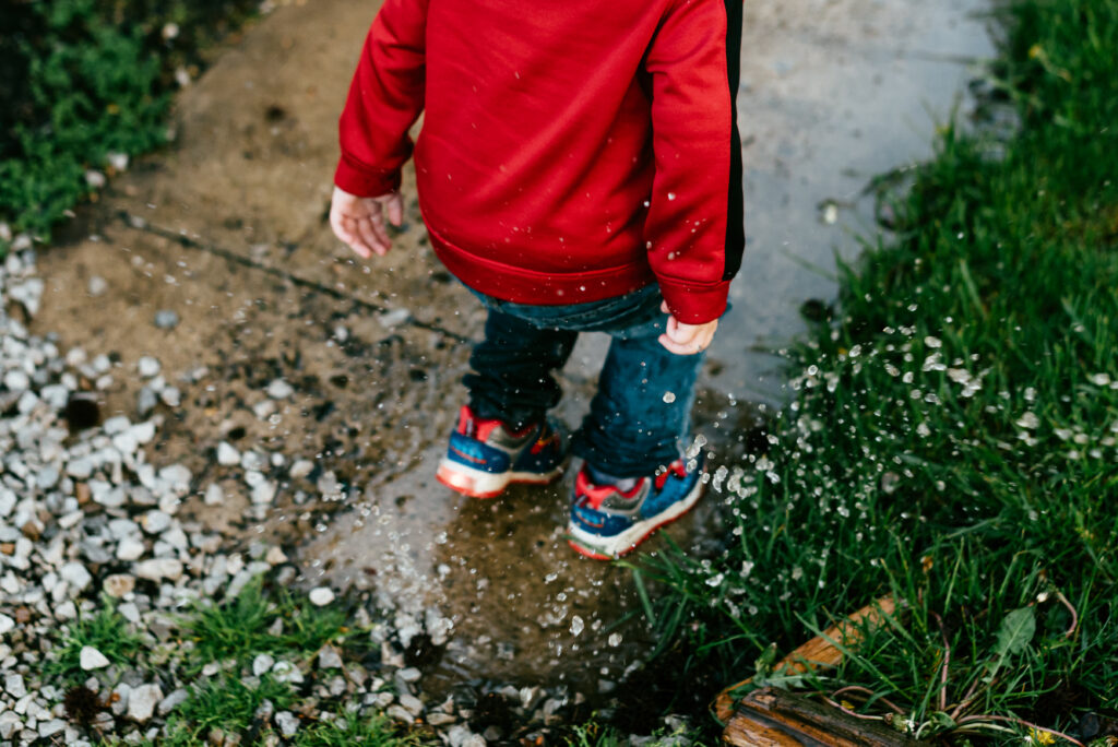 Child jumping in puddle on sidewalk